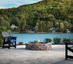 a fire pit sitting on top of a stone patio next to a forest covered hillside