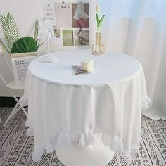 a white table cloth with ruffles on it and some plants in the background