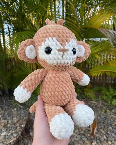 a small crocheted monkey is held in someone's hand with palm trees behind it