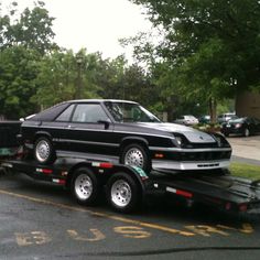 a black car is being towed by a flatbed trailer on the street in front of some trees