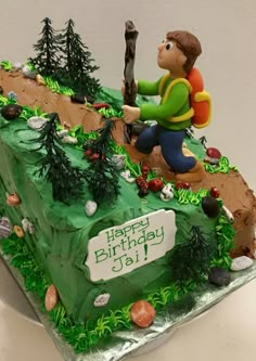 a green birthday cake with a boy holding a stick on top of the hill and trees