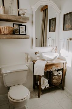 a white toilet sitting next to a bathroom sink under a mirror above a wooden vanity