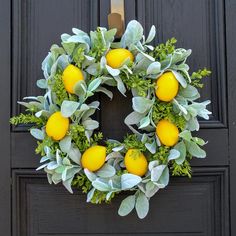 a wreath with lemons and green leaves hanging on a black front door, surrounded by greenery