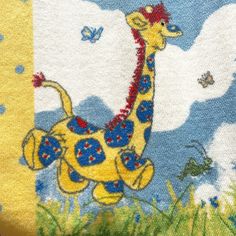 a yellow and blue towel with a giraffe on it's side in the grass