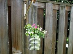 a metal bucket with flowers hanging from it's side on a wooden fence next to a planter