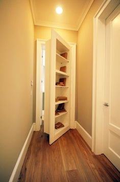 an empty hallway with white walls and wooden floors is pictured in this image, there are shelves on either side of the door