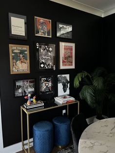 a table with two stools in front of a black wall covered in pictures and posters