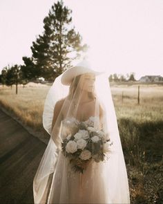 a woman in a wedding dress and veil walking down the road with flowers on her bouquet