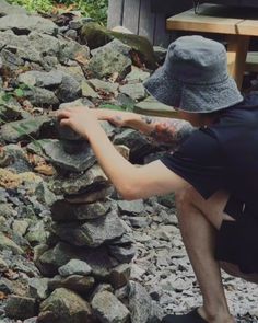 a man kneeling down next to a pile of rocks with a hat on his head