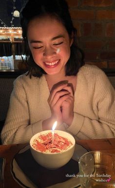 a woman sitting at a table in front of a bowl of food with a candle