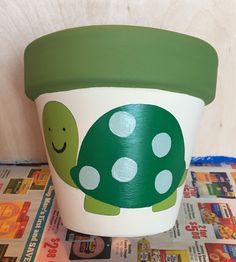 a green and white cup with a turtle painted on the side sitting on top of a newspaper