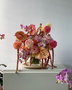 a vase filled with lots of colorful flowers on top of a white table next to a potted plant