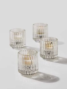 three clear glass candlesticks on a white surface with one candle in the middle