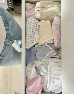 an open drawer filled with baby clothes on top of a wooden floor next to a person's feet