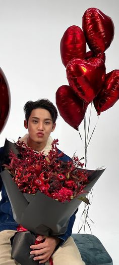 a young man holding a bunch of red flowers and heart shaped balloons in front of him