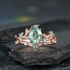 a ring with an oval cut green stone surrounded by leaves on top of a rock