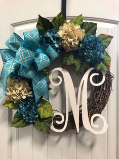 a wreath with blue flowers and green leaves on it is hanging on the front door