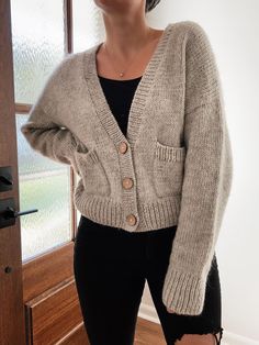 a woman standing in front of a door wearing a cardigan sweater and ripped jeans