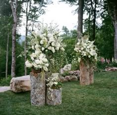 three wooden vases with flowers in them sitting on the grass next to some logs