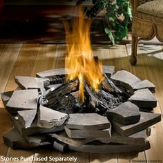 a fire pit made out of rocks and logs on a wooden floor with a plant in the background