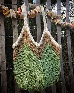 a crocheted bag hanging on a fence with sea shells and seashells