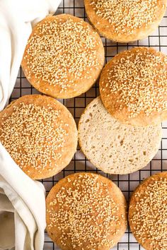 four sesame seed bread rolls on a cooling rack next to a white towel and napkin