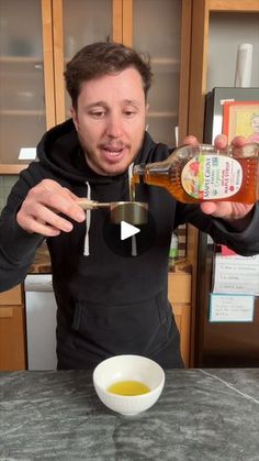 a man pouring honey into a bowl on top of a counter next to a cup