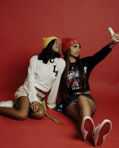 two young women sitting on the ground with their arms in the air