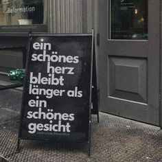 a black sign sitting on the side of a building next to a sidewalk and door