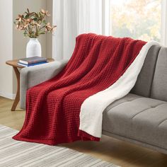 a couch with a red blanket on top of it next to a white vase filled with flowers