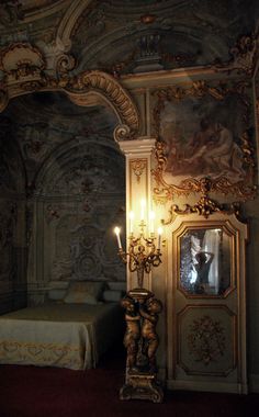 an ornately decorated room with a bed, mirror and table in the corner is lit by candlelight