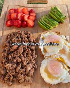 a wooden cutting board topped with eggs and meat next to sliced asparagus, strawberries and an avocado