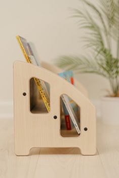 a wooden book holder with two books and pencils in it on a table next to a potted plant