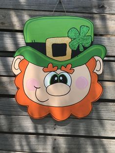 a st patrick's day sign with a green hat and clover on it hanging from the side of a wooden fence