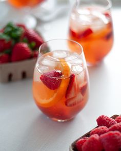 two glasses filled with liquid and fruit on top of a white table next to strawberries