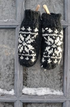 a pair of black and white knitted mittens hanging on a wooden door frame