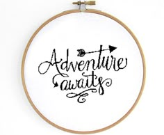 an embroidery hoop with the words adventure awaits in black ink on white paper and wood