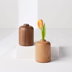 two wooden vases sitting on top of a white surface next to each other, one with a single flower in it