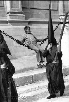 three people dressed in black holding flags and chains on their heads, one man is falling off the ground