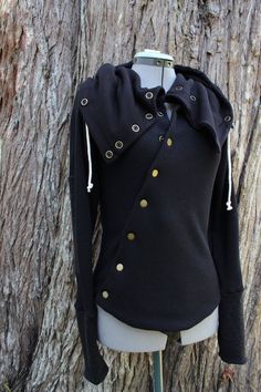 Black hooded cardigan, constructed from durable organic cotton thermal knit with black sweater knit accents and brass snaps. This hoodie features a diagonal snap-front detail across the chest, that continues up through its generous cowl neck/hood, which is adjustable with a drawstring and wood toggles. Solid brass snaps throughout. Two styles of pockets available at checkout. You can opt for a generous kangaroo pocket in the front OR have the front plain with a hidden pocket underneath the snaps Cotton Hoodie With Buttons, Cotton Hoodie With Buttons For Fall, Hooded Washed Black Outerwear With Pockets, Black Hooded Top With Pockets, Black Hooded Outerwear With Double-lined Hood, Hooded Washed Black Outerwear With Double-lined Hood, Black Cotton Sweater With Double-lined Hood, Hooded Cardigan, Cowl Neck