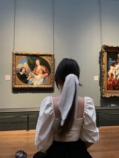 a woman sitting on the floor in front of two paintings with their backs to the camera