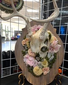 a deer's skull with flowers and antlers on a wooden stand in front of a tiled wall