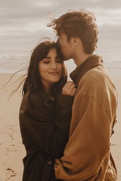 a man and woman standing next to each other on a beach with the ocean in the background