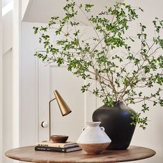 a table with two vases, a lamp and a book on it in front of a white wall