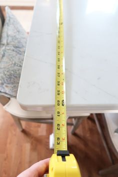 a person holding a tape measure in their hand near a table with chairs and a couch