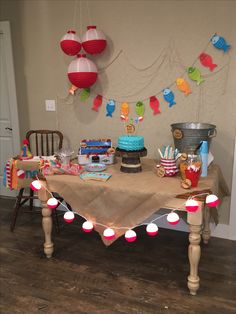 a table topped with lots of cake and cupcakes next to a wall hanging from the ceiling