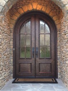 an arched wooden door with two sidelights and glass panels on the front entrance to a stone building