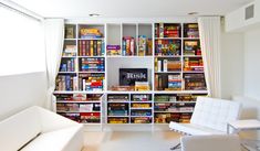 a living room filled with lots of white furniture and bookshelves on the wall