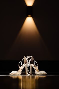 two pairs of white high heeled shoes sitting on top of a black table next to a lamp