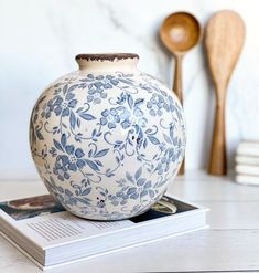 a blue and white vase sitting on top of a book next to wooden spoons